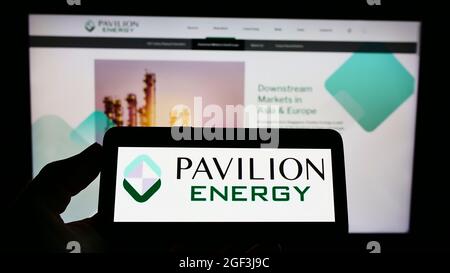 Persona che tiene il cellpohone con il logo della società Singaporian Pavilion Energy Pte. Ltd. Sullo schermo di fronte al sito web aziendale. Mettere a fuoco sul display del telefono. Foto Stock