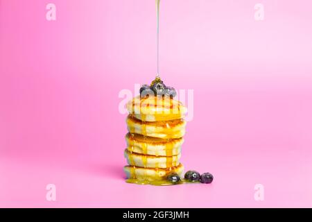 Pancake con frutti di bosco su sfondo rosa. Pancake deliziosi e lussureggianti con mirtilli e sciroppo per il brunch su uno sfondo minimal colorato. Bella foto di cibo luminoso. Foto di alta qualità Foto Stock