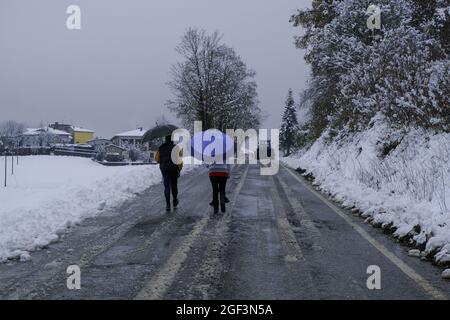 persone che camminano nella neve con ombrelloni e trattore pulizia strada nevosa attraverso il paesaggio rurale nevoso. Stagione invernale. Tempesta di neve Foto Stock