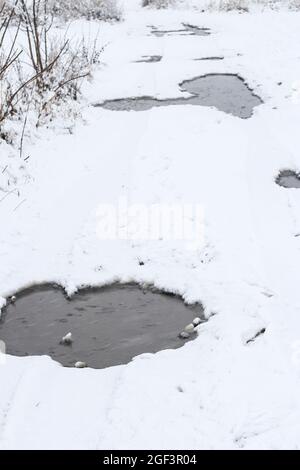 Pozzanghere su strada rurale coperta di neve in inverno durante la nevicata Foto Stock