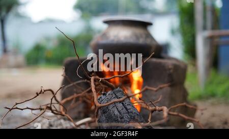 Blurred colpo, stufa indiana di cottura del terreno all'aperto di campagna di stufa o di stufa di creta di Chulha con un vaso circolare di colore nero su esso, Foto Stock