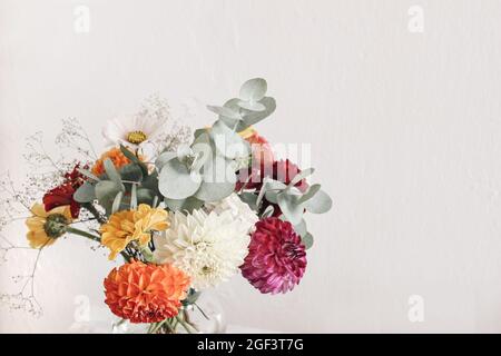 Bouquet bautiful di dahlia colorata, zinnia. COSMOS, fiori di gypsophila e rami di eucalipto. Sfondo della vecchia parete bianco sfocato. Floreale femminile Foto Stock