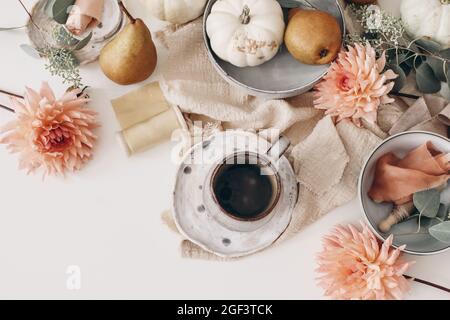 Composizione della vita morta d'autunno. Tazza di caffè, frutta di pera e zucche bianche. Fiori rosa di dahlia, eucalipto su sfondo bianco tavolo. Autunno stagionale Foto Stock