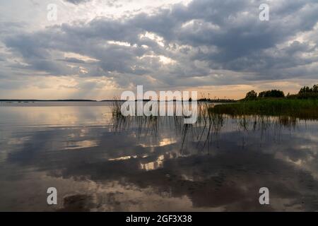 Un tramonto colorato e un'espressiva riflessione del cielo in un lago tranquillo e tranquillo con canne in primo piano Foto Stock