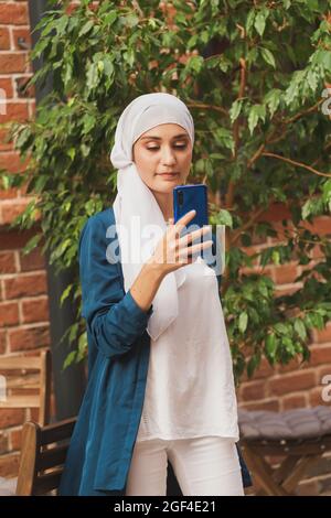 Donna musulmana che prende selfie. Bella ragazza felice con sciarpa prendere foto del suo auto utilizzando smartphone. Foto Stock