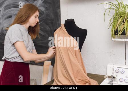 Sarta cerca su tessuto su un manichino nero in un laboratorio di cucito. Il designer disegna un abito dal tessuto beige e crea abiti abito femminile Foto Stock