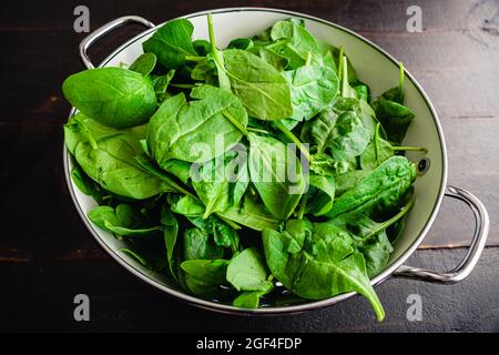 Spinaci freschi del bambino lascia in un colander: Un colander metallico riempito con le foglie fresche di spinaci del bambino Foto Stock