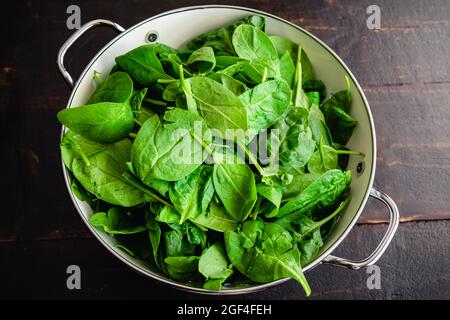 Spinaci freschi del bambino lascia in un colander: Un colander metallico riempito con le foglie fresche di spinaci del bambino Foto Stock