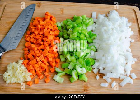 Vista dall'alto di verdure tritate su un tagliere di bambù: Carote tritate finemente, sedano, cipolle e aglio su un tagliere di legno con un san Foto Stock