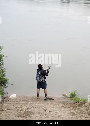 Pescatore che castano con un mulinello che gira accanto al fiume Foto Stock