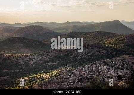 Uno scatto grandangolare o sfondo di un paesaggio stratificato drammatico di montagne rocciose con alberi al tramonto Foto Stock