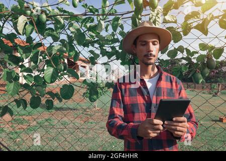 Uomo nero agricoltore che tiene una tavoletta con cappello in fattoria, frutto della passione pianta in background. Foto Stock