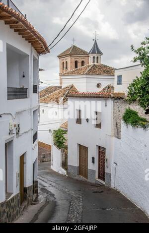 Strada spiovente del villaggio di Válor nell'Alpujarra con case bianche e la chiesa in stile Mudejar Foto Stock