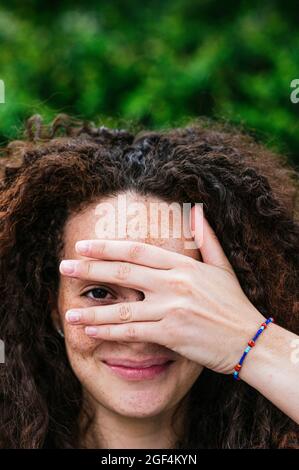 Sorridente donna ricci capelli che sbuccia attraverso le dita Foto Stock