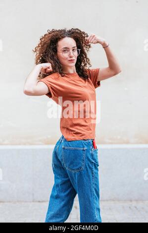 Fidata giovane donna puckering mentre flette i muscoli di fronte al muro Foto Stock