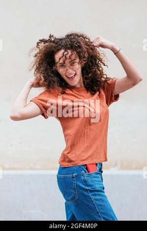 Giovane donna con capelli ricci che flettono i muscoli davanti alla parete Foto Stock