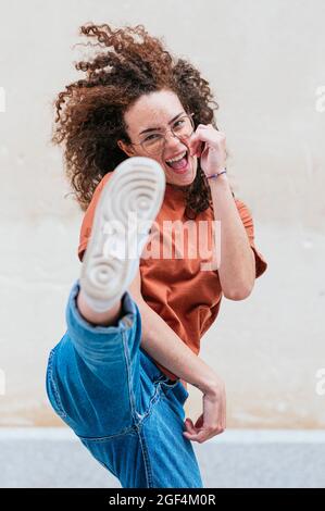 Giovane donna eccitata che calcia di fronte al muro Foto Stock