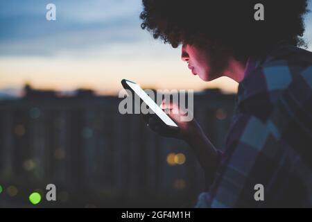 Giovane donna con capelli afro che usa smartphone all'aperto al tramonto Foto Stock