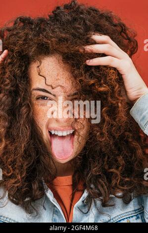 Giovane donna ricciola con le mani in capelli che si stacca fuori lingua Foto Stock