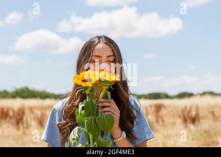 Giovane donna che puzzava di girasoli il giorno di sole Foto Stock