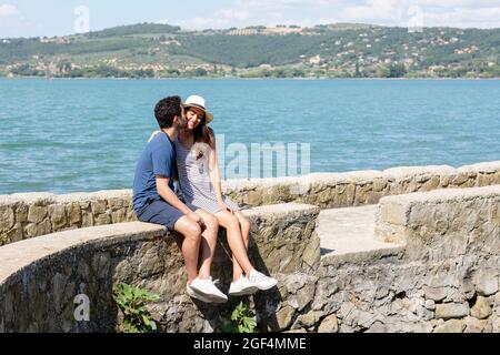 Uomo che bacia la ragazza sorridente mentre si siede sulla parete di ritegno Foto Stock