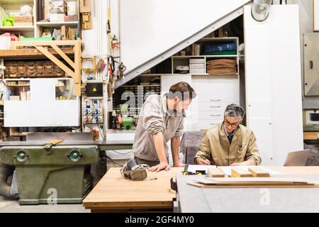 Proprietario e collega maturo che discutono al tavolo in officina Foto Stock