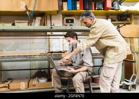 I carpentieri maschi discutono in officina su un computer portatile Foto Stock