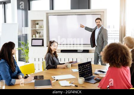 Professionista di sesso maschile che punta allo schermo di proiezione mentre lavora con un collega in riunione Foto Stock