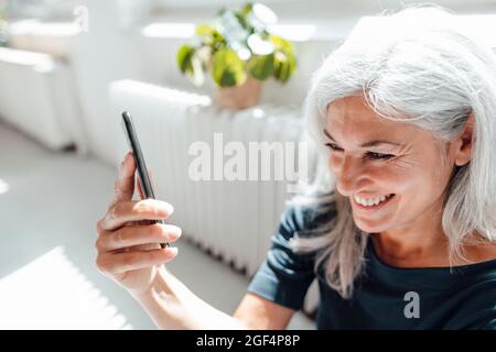 Donna d'affari sorridente che prende selfie attraverso il telefono cellulare in ufficio Foto Stock