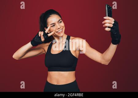 Sorridente sportivo gesturante segno di pace mentre prende selfie attraverso il telefono cellulare Foto Stock