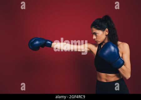 Fidata atleta femminile che pratica pugni di fronte al muro del maroon Foto Stock