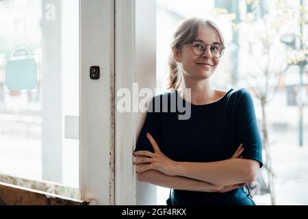 Giovane donna sorridente in piedi con le braccia incrociate alla porta Foto Stock
