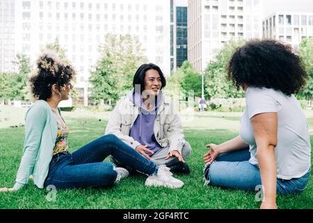 Giovane uomo che parla con amici multietnici di sesso femminile al parco Foto Stock