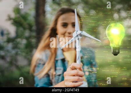 Donna che tiene il modello del mulino a vento vicino alla lampadina illuminata Foto Stock