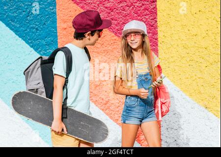 Amici maschi e femmine che usano il cellulare mentre camminano a muro Foto Stock