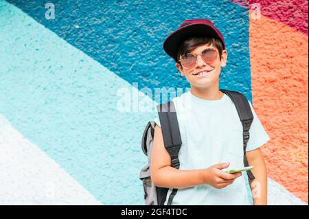 Ragazzo sorridente usando il telefono cellulare mentre cammina con il braccio intorno a un amico femmina a parete Foto Stock