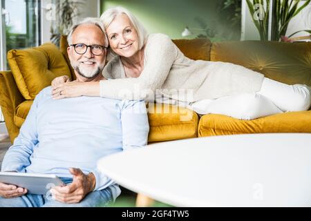 Donna sorridente che abbraccia l'uomo mentre riposa sul divano a casa Foto Stock
