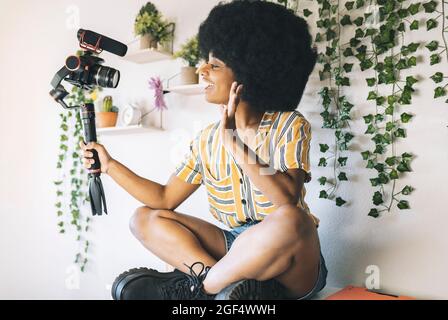 Il giovane influencer afro vacilla mentre vlogging attraverso la fotocamera a casa Foto Stock