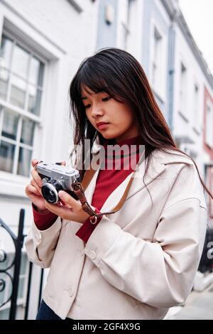Donna che utilizza una fotocamera analogica vicino all'edificio Foto Stock