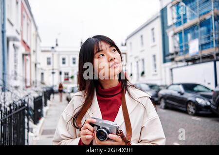 Donna pensierosa che tiene la macchina fotografica in città Foto Stock