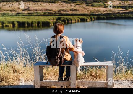 Donna con cane seduto su panca vicino al lago Foto Stock