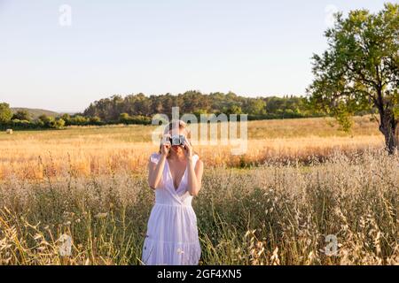 Giovane donna che fotografa attraverso la macchina fotografica nel campo Foto Stock