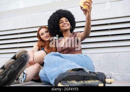 Sorridente Afro donna che prende selfie con un'amica di fronte al muro Foto Stock