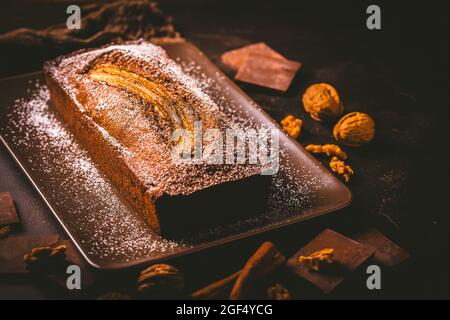 Pane di banana vegano fatto in casa o torta con noci, cioccolato e cannella su sfondo marrone Foto Stock