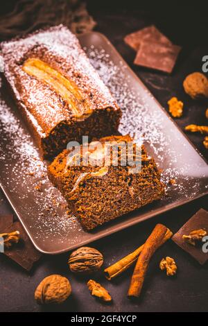 Pane di banana vegano fatto in casa o torta con noci, cioccolato e cannella su sfondo marrone Foto Stock