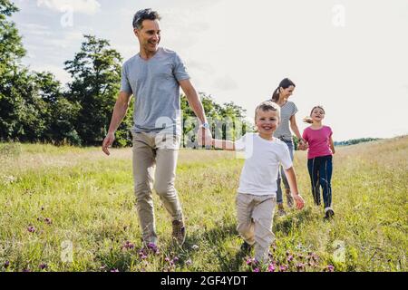 I genitori tengono le mani dei bambini mentre camminano sull'erba Foto Stock