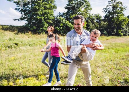 Il padre allegro che porta il figlio mentre cammina al prato Foto Stock