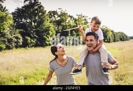 Madre che guarda il figlio seduto sulla spalla del padre durante la giornata di sole Foto Stock