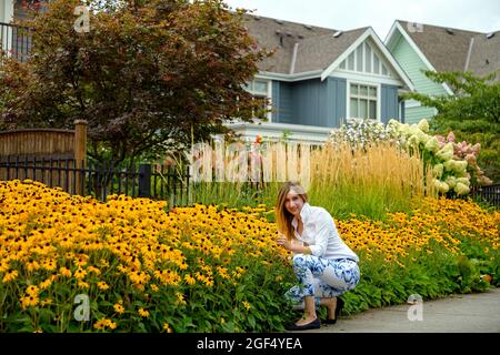 Felice donna attraente nel suo tardo 40s godendo il suo giardino di fiori bello e contently guardando la sua fioritura hortensia e fiori di ibisco dentro Foto Stock