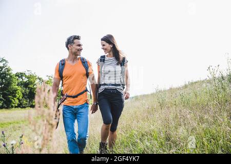 Coppia sorridente con zaini che parlano mentre si camminano sull'erba Foto Stock